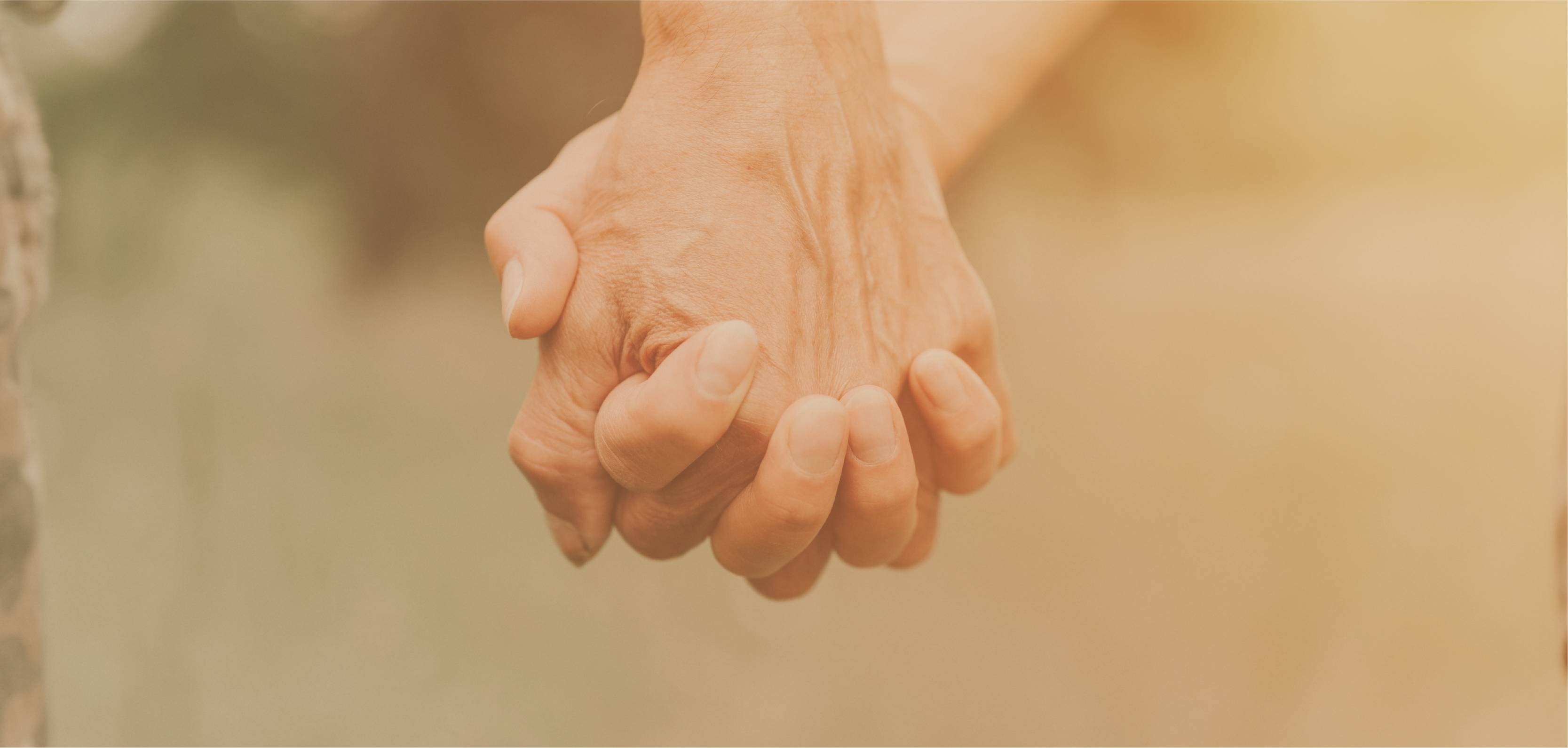 Close-up of two hands holding each other with a warm, blurred background